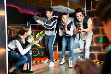 Ordinary Laser tag players young mens and womens playing in teams in dark laser tag station. High...