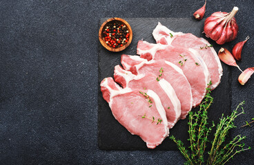 Raw pork chops, meat on slate board prepared for cooking with garlic, thyme, spices and pepper. Black kitchen table,  top view