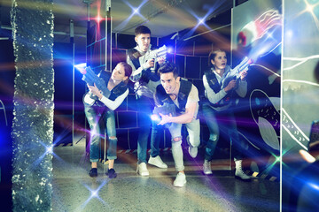 Modern satisfied pleasant smiling young people with laser pistols playing laser tag on dark...