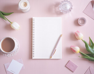 ピンクの背景にノートと花を並べた可愛いデスクイメージ