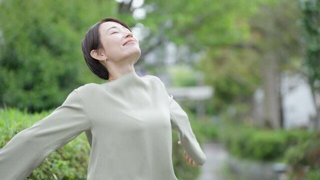 スローモーション　ストレッチするミドル女性（新緑・屋外・健康・ヘルスケア・伸び・深呼吸）