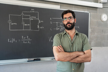 Young male teacher with beard standing alongside a chalkboard technology formulas. Teaching and...