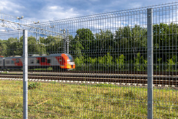 A metal fence behind which a train passes. Railroad fencing. Ensuring the safety of railway...