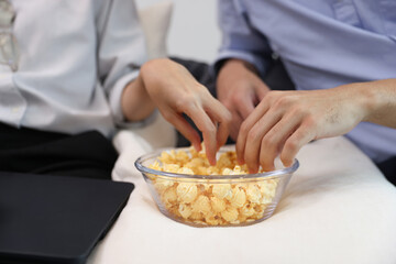 Close up hand of A couple  pick popcorn to eat , Young couple relaxation at home watching a movie and eating popcorn , enjoy and happy living at home concept