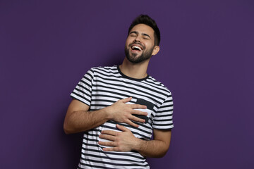 Young man laughing on purple background. Funny joke