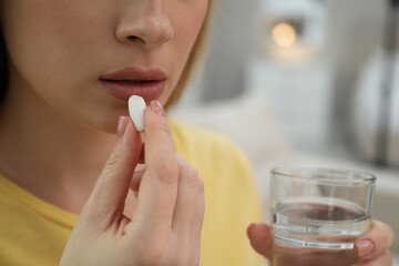 Young woman taking abortion pill on blurred background, closeup