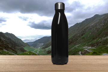 Black thermo bottle on wooden table and beautiful view of mountains