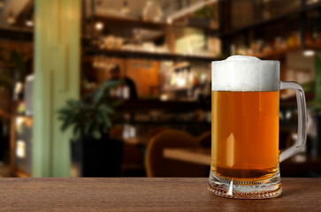 Glass mug with cold tasty beer on wooden table in pub, space for text