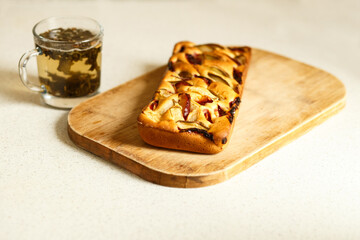 Autumn cake and a cup of tea. Autumn mood. Charlotte with apples and plums lies on a wooden board.