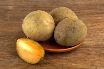 sapodilla fruit on a small plate with pieces of sapodilla fruit on a wooden background