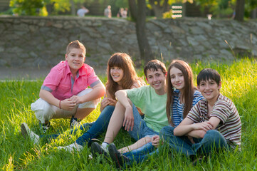 Teenagers boys and girls sitting on the meadow grass on a sunny summer day