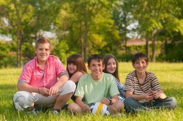 Fototapeta premium Teenagers boys and girls sitting on the meadow grass on a sunny summer day
