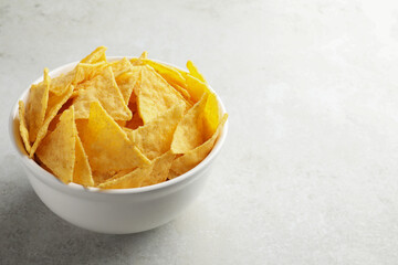 Bowl with tasty tortilla chips (nachos) on grey table. Space for text