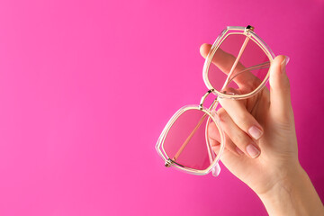 Woman holding stylish sunglasses on pink background, closeup of hand. Space for text