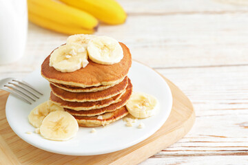 Plate of banana pancakes served on white wooden table, closeup. Space for text