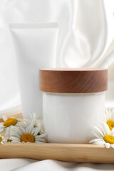 Different hand care cosmetic products and chamomiles on white silk fabric, closeup