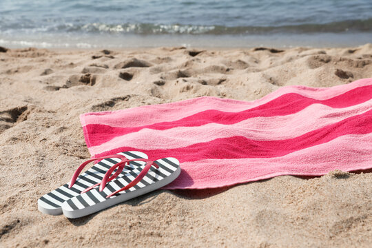 Pink striped towel with flip flops on beach sand near sea