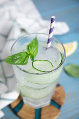 Glass of refreshing cucumber water with basil on light blue wooden table, closeup
