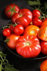 Many different ripe tomatoes with leaves on black table, closeup
