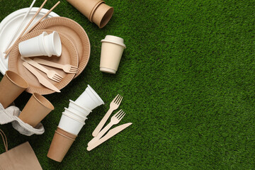Eco disposable tableware on green artificial grass, flat lay. Space for text