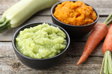 Tasty puree in bowls, zucchini and carrots on wooden table, closeup