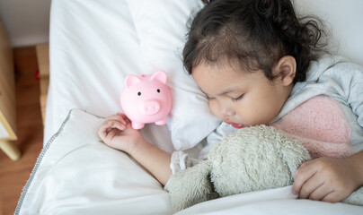 Caucasian Cute female child sleeping on a piggybank on bedroom.Baby taking a nap and a piggy bank.Childcare cost life insurance.