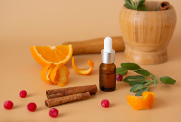 Bottle with essential oils and ingredients: orange, cinnamon, sage on a beige background