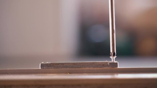 A Phillips screwdriver unscrews a shiny screw from a metal part close-up on a blurred background. The process of dismantling and dismantling structures in everyday life