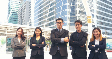 Fototapeta premium Group of business people asian team partners walking in city happy together. Leader executive men standing at modern urban city with confident teamwork. Portrait diversity businesspeople teamwork