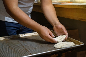 Baker's hands placing bread on a tray to be baked.