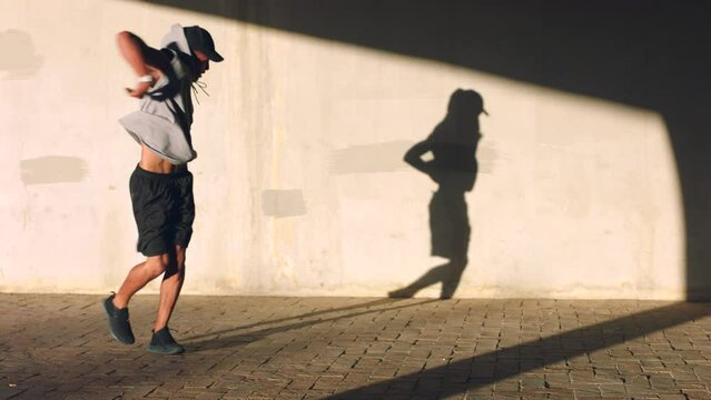 Dance, music and energy with a man dancer dancing outside for training and practice with his shadow on a wall. Fitness, freedom and hip hop with a young male performer or artist doing choreography