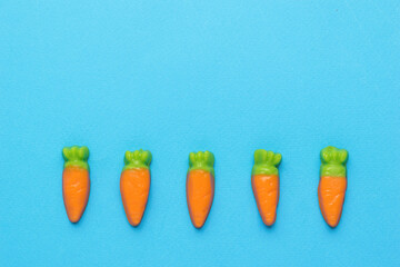 Small candy in the form of carrots on a blue background. Minimal harvest concept. Creative photo.