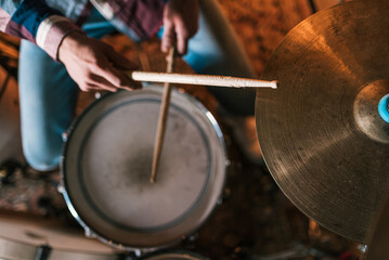 High angle of crop anonymous male musician with wooden drumsticks playing rock music on drum set on stage