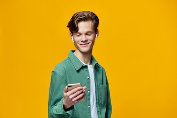 a guy in a green t-shirt stands with a phone in his hands on a yellow background