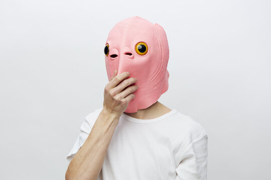 a man in a funny pink mask covers his mouth with his hand while standing on a light background