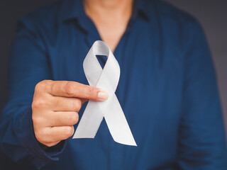 Close-up of hand holding a white ribbon on a gray background - obrazy, fototapety, plakaty