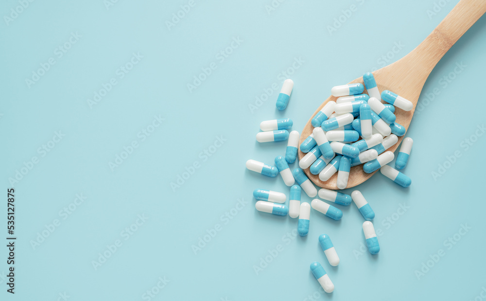 Wall mural top view of blue-white antibiotic capsule pills on wooden spoon and blue background. antibiotic drug