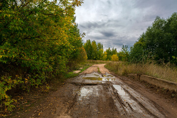 Broken country road with puddles against the background of an autumn stormy landscape