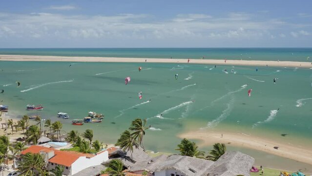 Luxury homes and resorts line the shore at Guajiru Island in Brazil. Hundreds of people enjoy kitesurfing in the shallow water. 