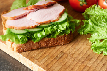 A sandwich with slices of smoked meat and juicy herbs, close-up.