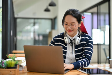Attractive young Asian female student using laptop, remote working at the cafe.