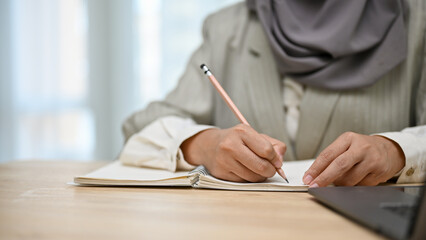 cropped, Bright Asian Muslim female college student writing something on her notebook.