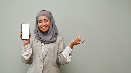 Attractive Asian Muslim woman wearing hijab showing a smartphone white screen mockup