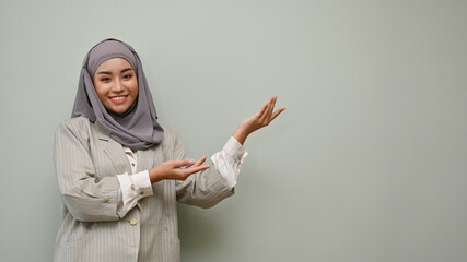 Beautiful Asian Muslim woman standing with open palm over isolated grey background.