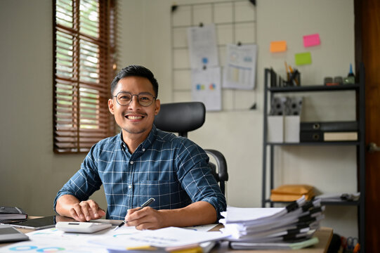 Handsome smart and happy millennial Asian businessman working at his office desk