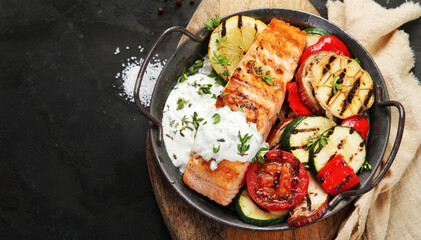 Salmon steak with vegetables and white sauce on dark background.