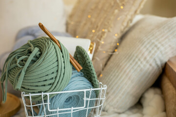 Closeup green ribbon yarn clew with scissors and crochet needles assembling into metallic basket...