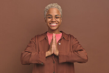 Young happy attractive African American woman joins palms in front of chest makes Namaste gesture...