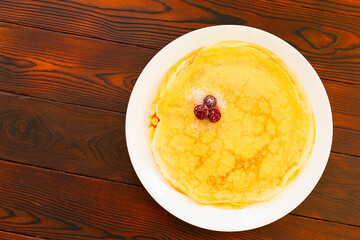 Traditional slavic pancakes or crepes on white plate, decorated with cherry and sugar. On wooden table top. Flat lay. 