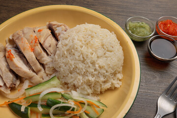 steamed Hainanese chicken rice green red chilli ginger soya sauce cucumber carrot side serviced on retro enamel diner plate fork spoon on wooden table